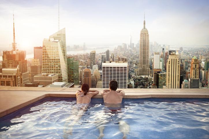 夫妇在酒店屋顶的游泳池放松，俯瞰令人印象深刻的纽约天际线.